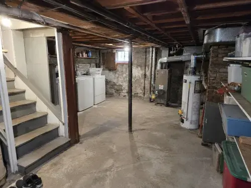 Cape Cod basement before guest-suite planning with low ceiling, laundry, ducts, posts, and utilities.