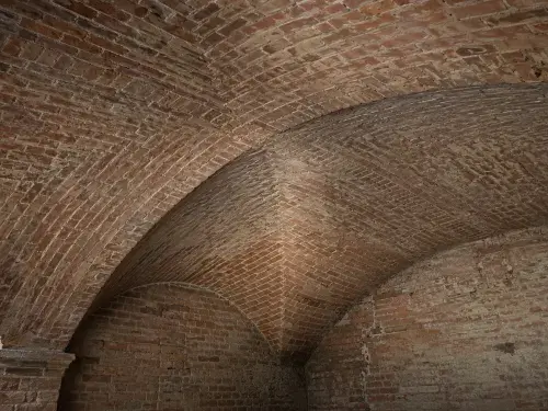 Close view of a brick groin vault showing the diagonal intersection of two curved vault surfaces.