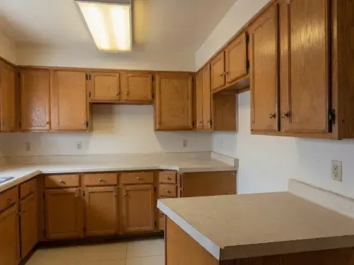 Dated empty kitchen with oak cabinets, laminate counters, and fluorescent lighting.