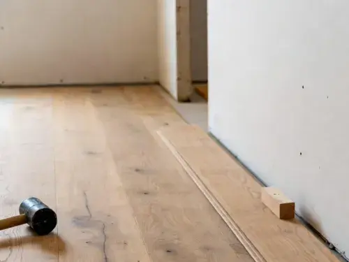 Installing unfinished hardwood flooring along a wall edge.