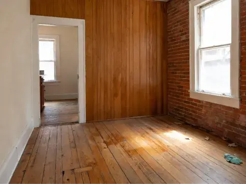 Worn hardwood floor in an old room beside exposed brick and wood paneling.
