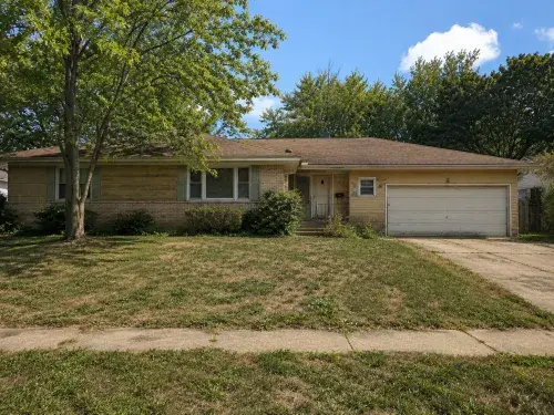 Dated brick ranch house with an attached garage, overgrown shrubs, and a worn front yard.