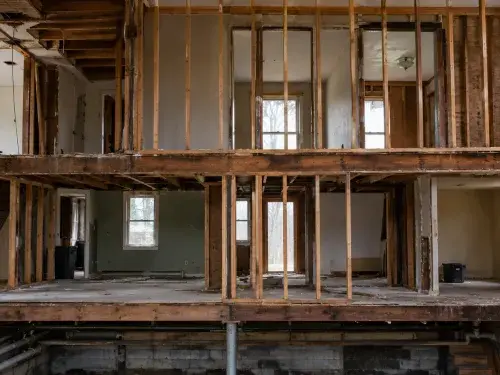 Two-story house renovation with exposed framing and basement support below.