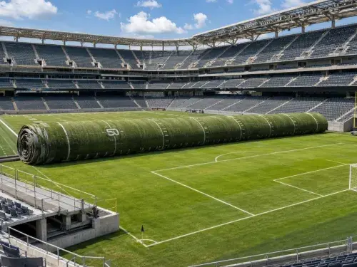 American-football field rolling away to reveal a natural-grass soccer pitch inside an existing stadium.