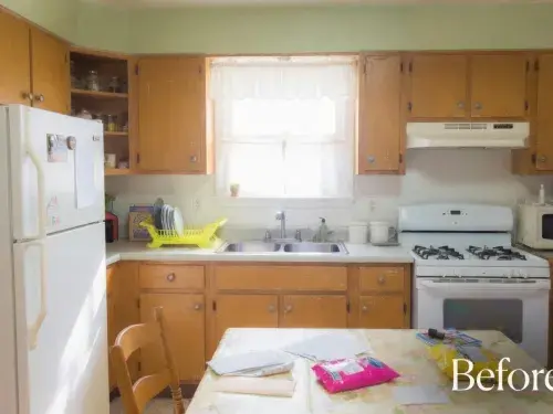 Worn midcentury kitchen with wood cabinets, white appliances, and a crowded dining table.