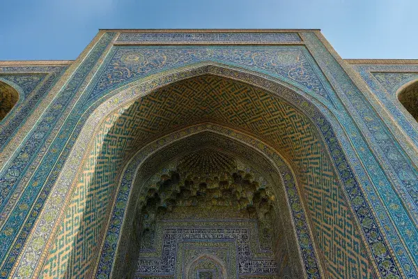 Upward view of an Islamic archway with muqarnas vaulting and blue geometric tile patterns.