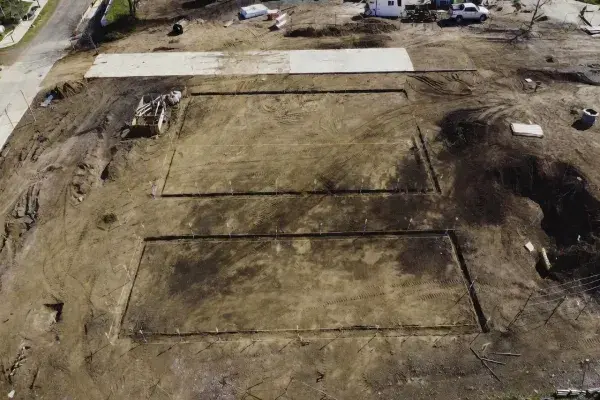 Prepared residential building site with layout stakes, early access concrete, and graded ground before construction starts.