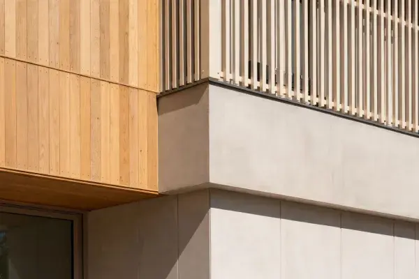 Facade junction combining timber cladding, vertical screening, and light mineral-finish wall surfaces.