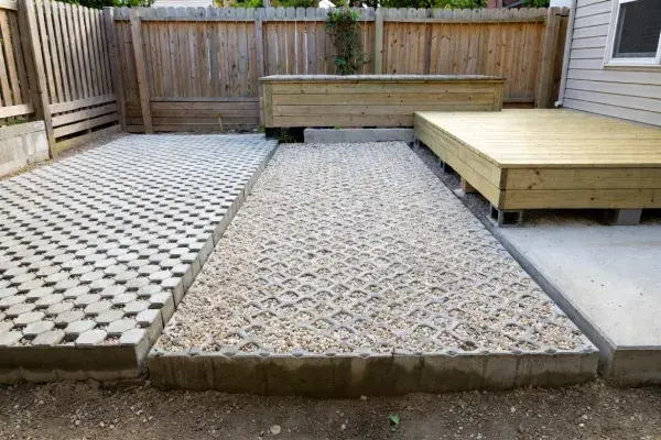Permeable pavers, gravel grid, and a raised timber platform used as slab alternatives in a yard.