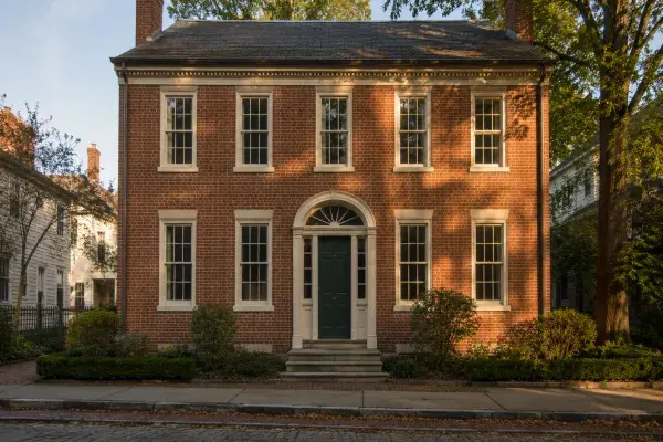 Federal-style brick house with a symmetrical facade, tall sash windows, centered entry, fanlight, sidelights, and restrained white trim in warm sunlight.