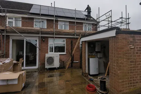 Solar panels, heat pump, and battery equipment being installed at a UK brick house.