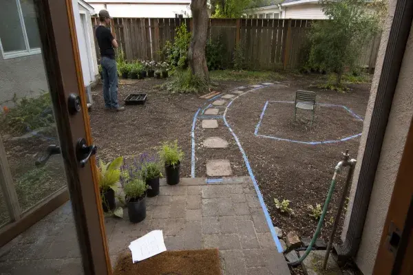 A home garden being planned from the back door with path, seating, plants, and water access marked before planting.