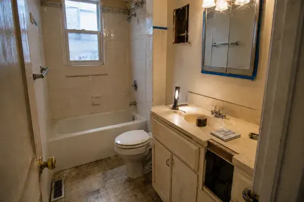 1960s bathroom before remodel with old wall tile, tub-shower, worn flooring, dated vanity, open access area, flashlight, tape measure, and sample tile.