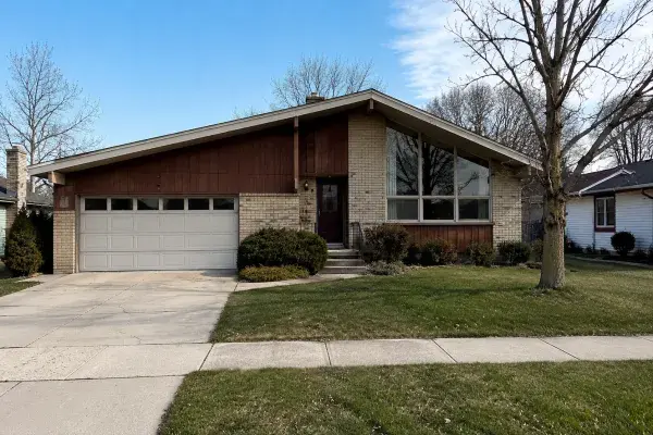 Modest 1970s suburban house with brick, wood siding, attached garage, and dated entry.