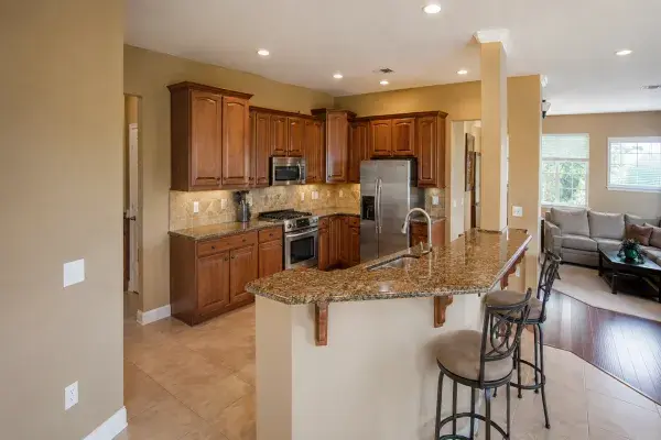 Early 2000s builder kitchen with cherry cabinets, brown granite, tile floor, and open family room.
