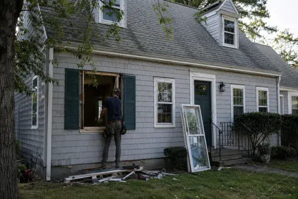 Cape Cod house during window replacement with an open window bay and worker outside.