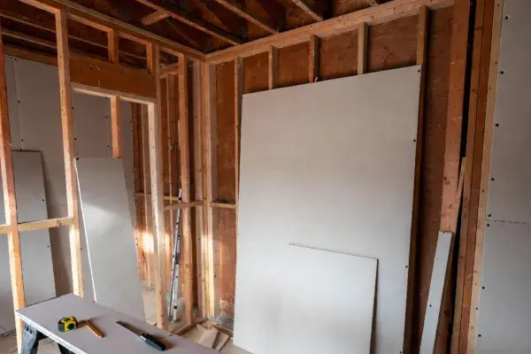 Drywall sheets staged in a renovation room before installation with exposed framing and layout tools.