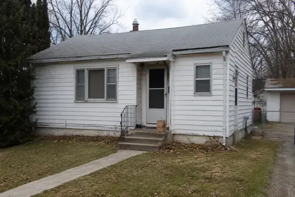 Plain 1950s bungalow exterior before renovation with dated siding, small stoop, and modest windows.