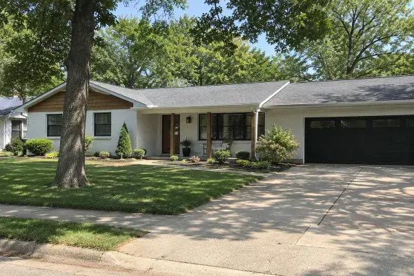 Renovated 1980s ranch house with attached right-side garage and shaded front lawn.