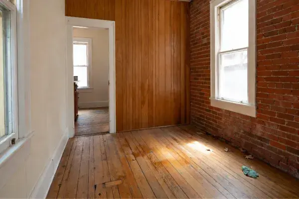 Worn hardwood floor in an old room beside exposed brick and wood paneling.